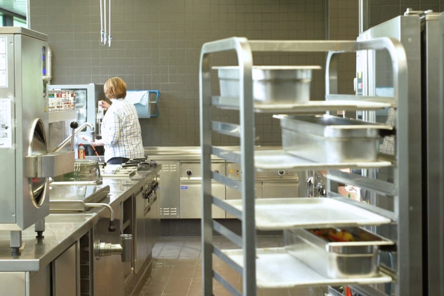 Blick in eine Küche mit Servierwagen im Vordergrund und Mitarbeiterin im Hintergrund