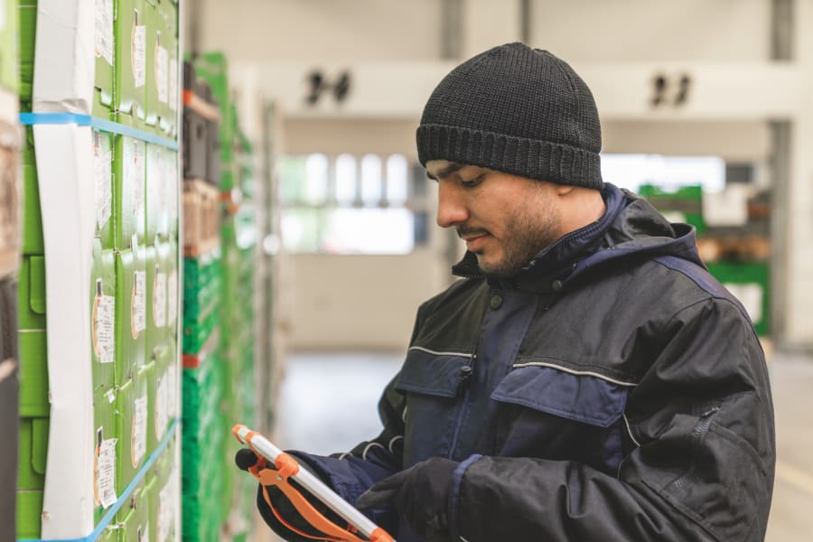 Mitarbeiter mit Mütze der ein Tablet hält und etwas prüft